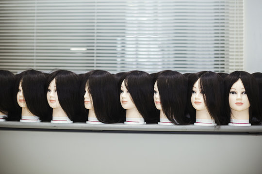 Large group of mannequin heads with brown wigs in a row on a table.