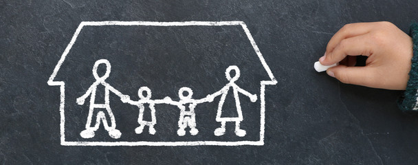 Enfant dessinant une famille dans une maison à la craie sur une ardoise