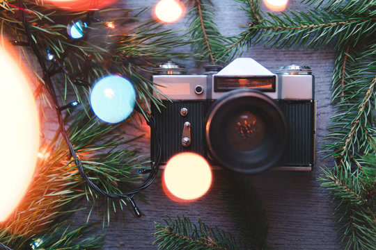 Retro Camera And Christmas Blank Photo Frame With Fir Tree Branches, Decorations Colour Lights Bokeh Wooden Background. Mock Up. Flat Lay. Top View