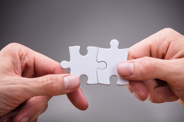 Close-up Of Businesspeople Holding Jigsaw Puzzle