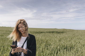 Young woman using smartphone, standing in field