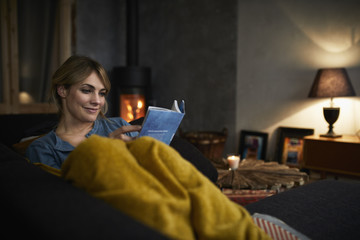 Portrait of smiling woman reading a book on couch at home in the evening