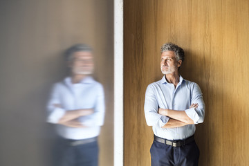 Reflection of mature businessman standing at wooden wall