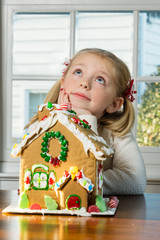 adorable school age girl decorating gingerbread house during Christmas 