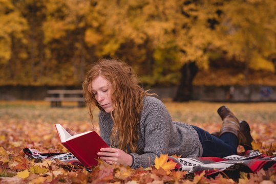 Woman lying in the autumn park and reading novel