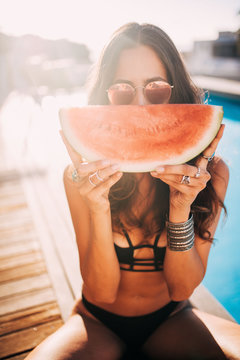 Woman holding watermelon while sitting at swimming pool during summer