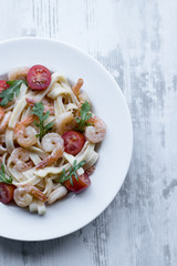 Delicious carbonara with tasty pawns and arugula in a white plate on grey wooden background.
