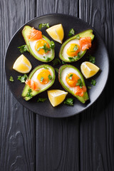 Baked avocado with egg, smoked salmon and greens close-up on a plate on a table. Vertical top view