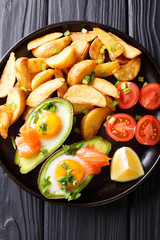 Delicious food: Baked avocado stuffed with eggs and salmon, fresh tomatoes and potato close-up. Vertical top view