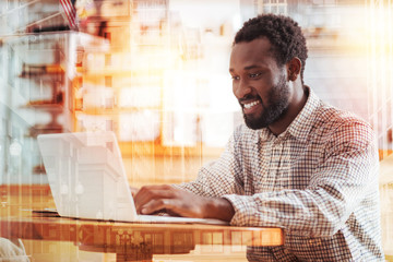 Work with pleasure. Delighted bearded man keeping smile on his face and leaning arms on the table while looking forward