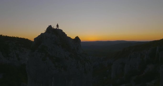 Aerial wide shot of a man celebrating on the top of the mountain in beautiful evening light.
