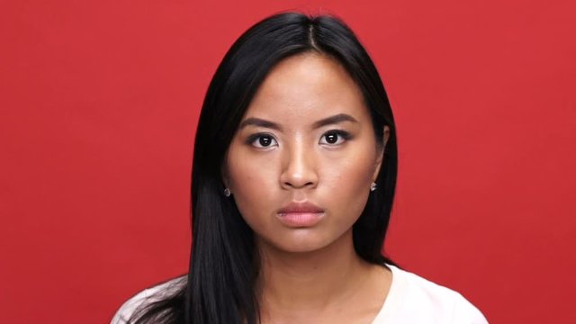 Close up view of displeased asian woman in t-shirt looking around over red background