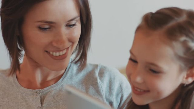 Young attractive brown-haired woman spending time with daughter. Beautiful girls watching comedy on digital tablet. Close-up.