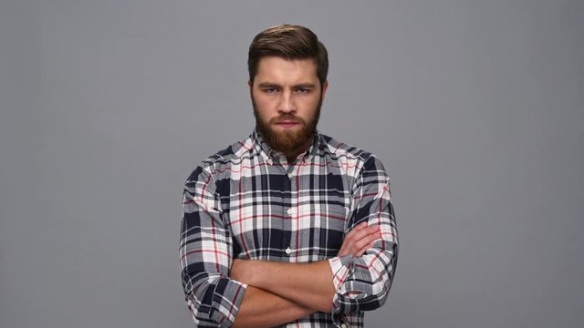 Angry serious bearded man in shirt with crossed arms looking at the camera over gray background
