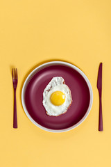 Scrambled eggs on a maroon dish with burgundy cutlery on a light yellow background..