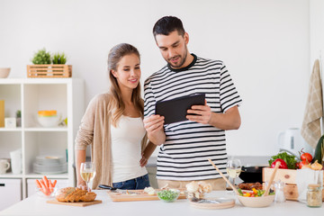happy couple with tablet pc cooking food at home