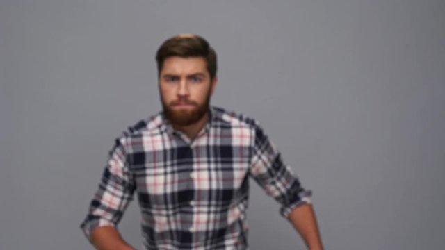 Mystery bearded man in shirt sneaks, looking at the camera and running away after that over gray background