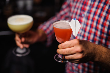 man holds two alcoholic cocktails of yellow and red colour