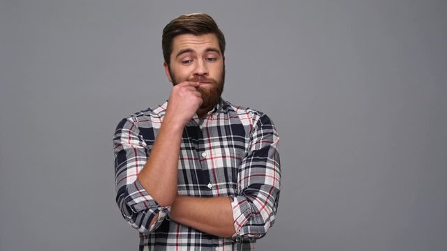 Thoughtful bearded man in shirt looking around over gray background