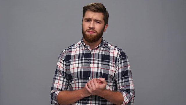 Confused bearded man in shirt upset and looking down over gray background