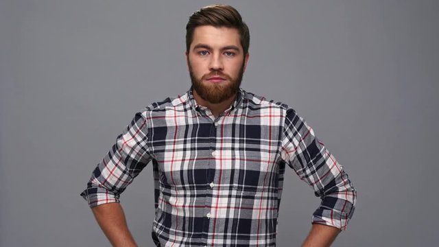 Surprised bearded man in shirt looking at the camera and upset after that over gray background