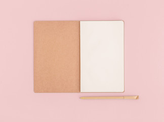 Fototapeta premium Notebook opened and a pen on a pink desk. Flat lay.
