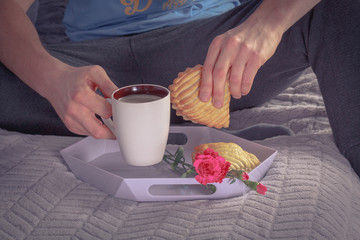 Man in tracksuit sitting on bed and drinking coffee and eat cookie with apple. Photography with vintage filter.