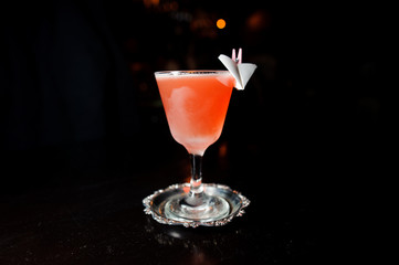 alcoholic cocktail of pink color stands on a special plate on a black background