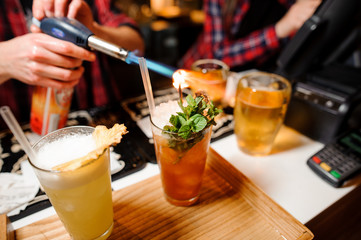 barman sets fire to sprig of mint on orange-colored cocktails