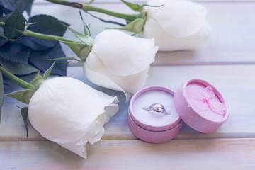 The concept of Love, Wedding, Proposal, Anniversary, St. Valentine's Day, Mother's Day with beautiful white roses and a wedding ring in a box in a close up, light wooden background