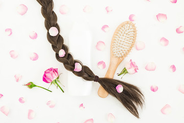Beauty composition with comb for hair styling, shampoo and pink flowers on white background. Flat lay, top view