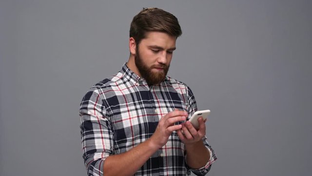 Smiling bearded man in shirt using smartphone over gray background