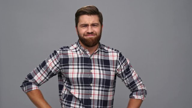 Displeased bearded man in shirt showing thumb down over gray background