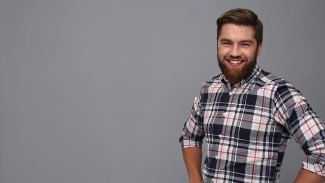Happy bearded man in shirt with crossed arms pointing away and showing thumbs up over gray background