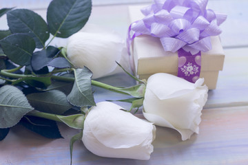 The concept of Love, Wedding, Proposal, Anniversary, St. Valentine's Day, Mother's Day with beautiful white roses and a gift box with a ribbon in a close up, light wooden background