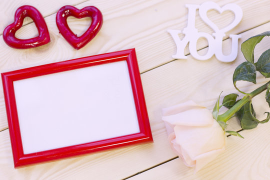 Concept of St.Valentine's Day, Love, Anniversary, Wedding with a pale cream rose, I love you inscription and a red photo frame, natural wooden background, top view