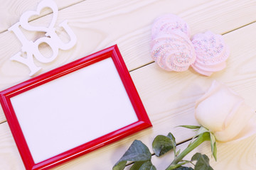 Concept of St.Valentine's Day, Love, Anniversary, Wedding with a pale cream rose, I love you inscription and a red photo frame, natural wooden background, top view