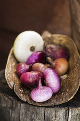 A lot of garden sweet red and white onions in an antique vintage wooden ladle on a simple wooden background. The concept of simple organic natural beneficial products for family meals. Vertical