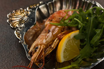 One fried large tiger shrimp head on with lemon and rukkola on ancient plate
