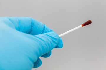 Hand in blue glove holding tweezers with a cotton bud