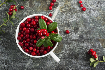 Fresh ripe forest northern cranberries or cowberry, lingonberry in ceramic cups of different size and color on a gray stone aged background for the concept of organic natural healthy food. Top View.