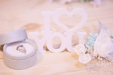 Concept of St.Valentine's Day, Love, Anniversary, Wedding with I love you inscription, a ring in a blue box and a decoration with flowers in a close up, light blurred background