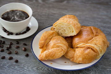 Butter Croissants in white dish and hot black coffee in the cup  and coffee seeds on wooden table
