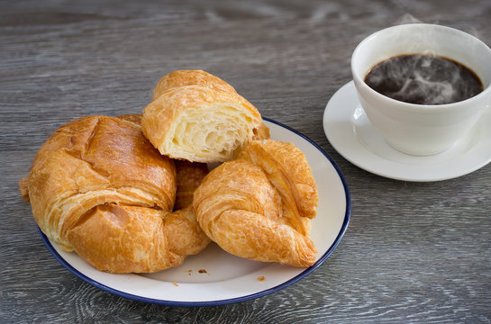 Butter Croissants in white dish and hot black coffee in the cup  on wooden table
