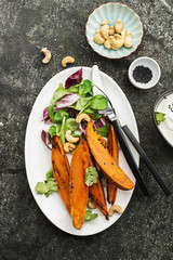 Baked slices of sweet potatoes for a vegetarian healthy snack lunch with salad, yoghurt sauce, black sesame served portioned in a plate. Top View.