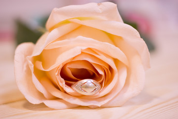 The concept of Love, Proposal, Wedding, Anniversary, Birthday with a ring in a pale cream rose on a wooden table, close up