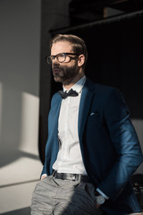 handsome stylish young businessman in eyeglasses and bow tie looking away