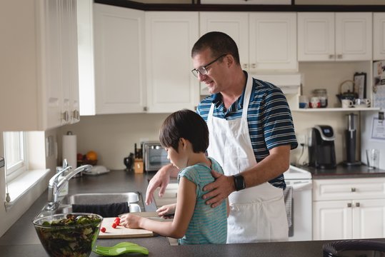 Attentive father helping his son to cut vegetables 