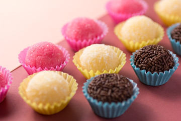 Brigadeiro, Beijinho and Bicho de Pe: sweets from Brazil. Child birthday party. Candy balls in a straight line. Colorful background.