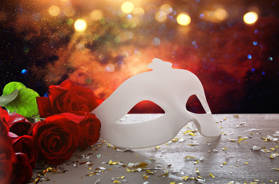 Image of elegant venetian mask and red roses over wooden table